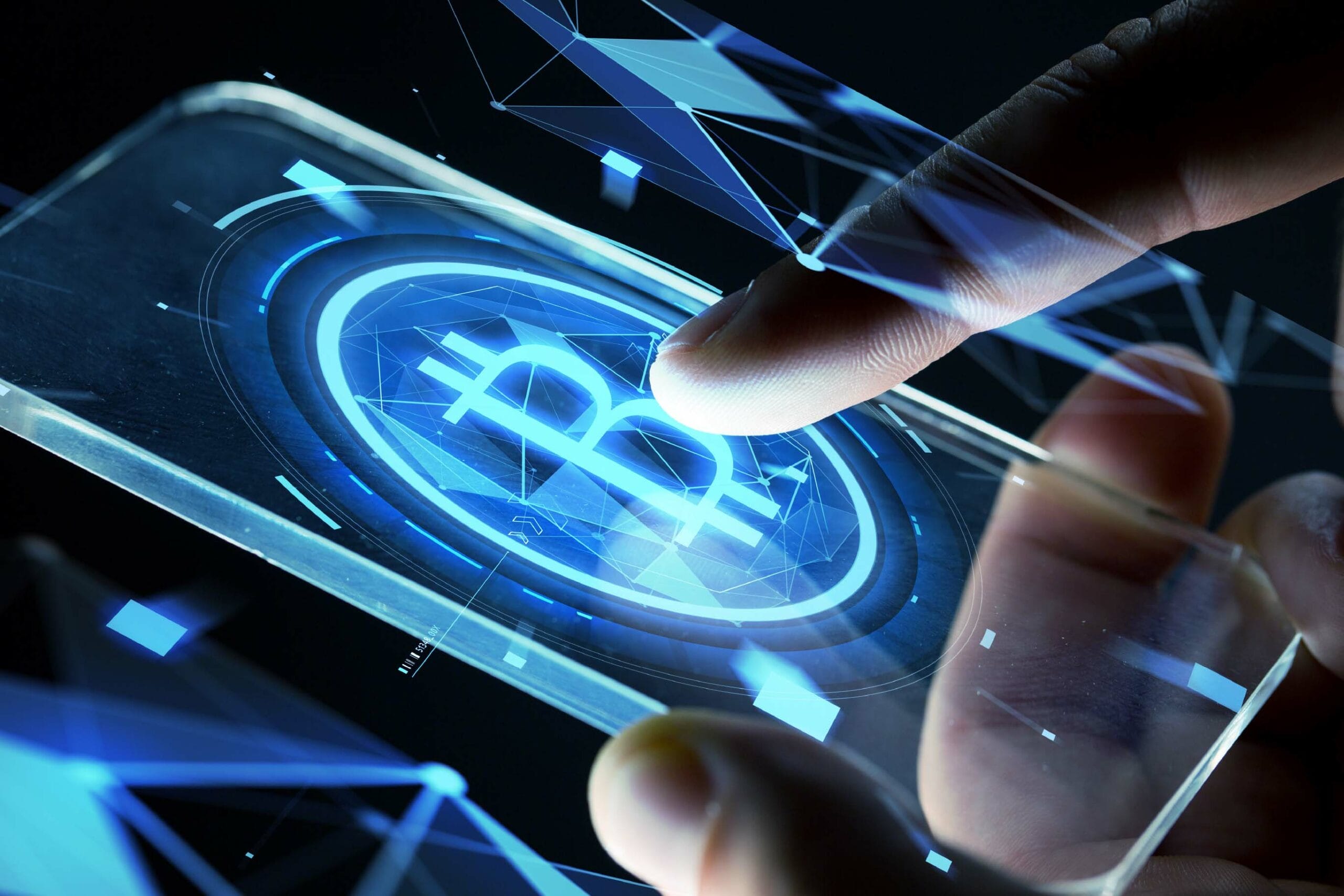 A close-up of hands holding a transparent digital device or screen displaying a glowing blue Bitcoin symbol. The image has a futuristic feel with holographic-style interface elements and geometric lines radiating from the Bitcoin logo.
